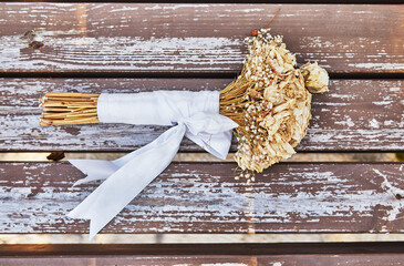 Bouquet of dried roses tied with white ribbon lying on bench at sunset