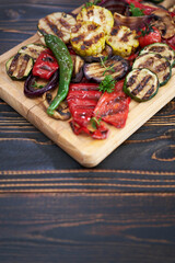 Grilled vegetables mix on a wooden cutting board - zucchini eggplant onions corn mushroom tomato