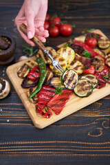 Grilled vegetables mix on a wooden cutting board - zucchini eggplant onions corn mushroom tomato