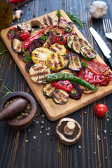 Grilled vegetables mix on a wooden cutting board - zucchini eggplant onions corn mushroom tomato