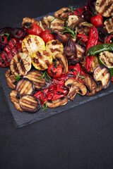 Grilled vegetables mix on a stone serving board - zucchini eggplant onions corn mushroom tomato