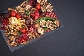 Grilled vegetables mix on a stone serving board - zucchini eggplant onions corn mushroom tomato