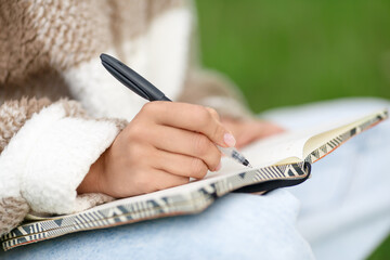 Close-up view of a female hands writing notes with pen while sitting in the street.