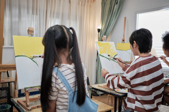 Group of multiracial little children concentrates on acrylic color picture painting on canvas in an art classroom and creatively learns with talents and skill at elementary school studio education.