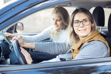 Beautiful best friends joyfully leave city sitting into car salon. Young women with happy mood go...