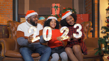 An African American black family, woman, father, mother and kid girl with 2023  new year, present gift in party on Merry Christmas Eve Xmas on holiday. Celebration at home. People lifestyle.