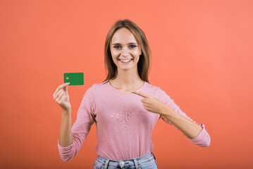 The girl points her finger at a credit card with a copy space for advertising on a red background.