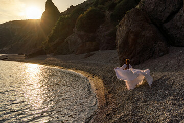 A mysterious female silhouette with long braids stands on the sea beach with mountain views, Sunset...