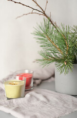 Fototapeta na wymiar glowing candles on linen textile next to cement vase with pine tree branch. aesthetic composition home decor and cozy ambience. vertical