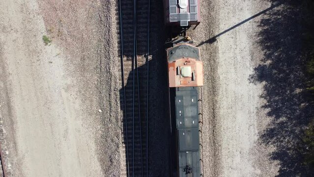 Top down aerial footage from a drone looking straight down at a train that is moving from the top of the shot to the bottom with big shadow.