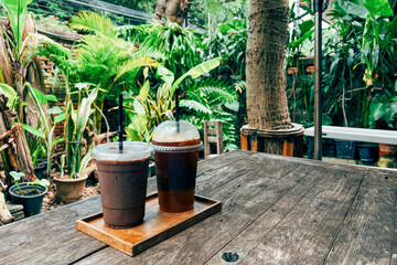cold mocha coffee in plastic cup on wooden table in cafe with plant and sunlight background. glass...
