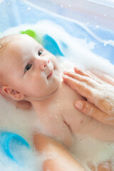 Baby bath time. Close-up detail view of mother bathing cute little peaceful baby in tub with water...