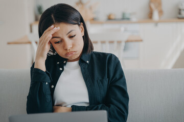 Tired overworked woman freelancer working at laptop, holding head reads email with bad news at home