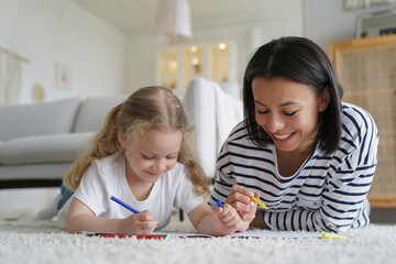 Happy mom, adopted daughter drawing together, lying on floor. Adoption, children's creative leisure