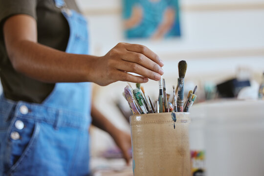 Woman, artist and hand of painter reaching for paintbrush in studio, creative workshop or art class painting. Closeup of female doing artwork and craft as hobby with a brush set or collection inside