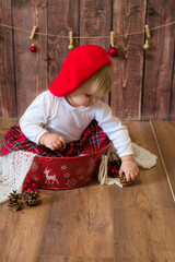 
A little cute girl in a red plaid skirt and a red felt beret plays with cones and Christmas toys in a room decorated for Christmas. Christmas and children