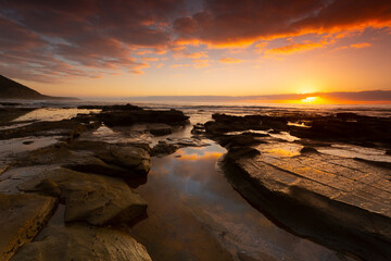 Stunning sunrise highlighting clouds and  over the ocean with rock pool reflections on the sea shore