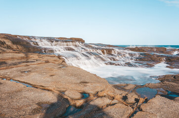 Milky ocean cascades flowing over honey coloured rocks