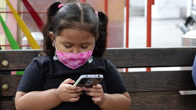 Asian little girl sitting while playing cellular phone or smartphone or gadget in public space