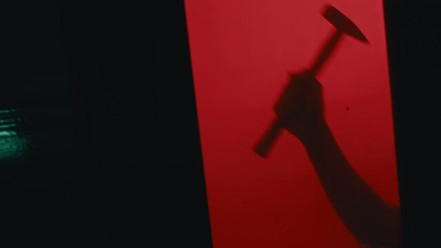 Silhouette of a hand holding a hammer behind a glass door and red background