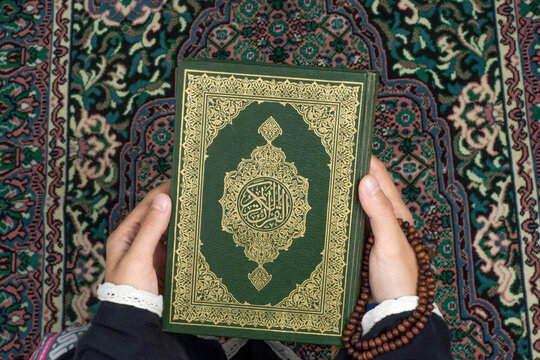 The Koran is held by a woman on a prayer rug