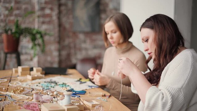 Two jewelry designers working in studio with tools making gemstone necklaces, bracelets and earrings. Female friends crafting jewellery together