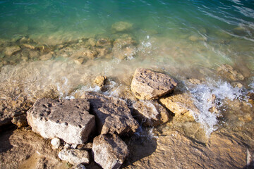 Waves from a clear blue lake crashing on rocks.