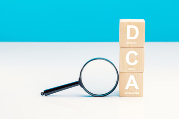 Magnifying glass and DCA word on a wooden cube in idea Dollar Cost Averaging investment strategy, Saving stock or savings on a monthly, quarterly basis.