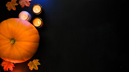 Pumpkin, burning candles and autumn leaves on a black background. Festive background with place for...