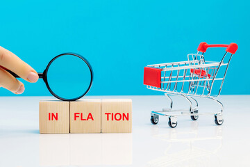 Financial leverage and wealth balance during inflation concept. Letter blocks with word inflation with a magnifying glass in woman's hand near empty shopping cart on blue background.