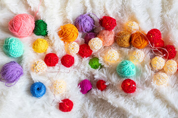 A lot of colorful knitting yarn and a luminous garland in the form of balls lie on fluffy blanket.