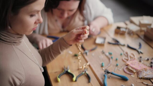 Two jewelry designers working in studio with tools making gemstone necklaces, bracelets and earrings. Female friends crafting jewellery together