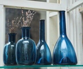 A blue glass vase with a dry plant is on the shelf. Next to it is a jug made of the same material....