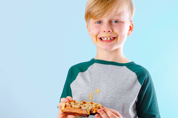 Portrait of a child eating a sweet Belgian waffle on a blue background. Dirty sweet pistachio sauce...