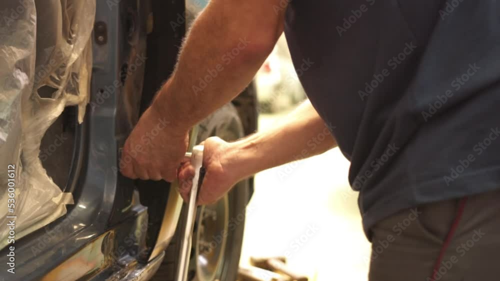 Poster mechanic with a wrench fixing the side of a car that has been broken due to a car crash