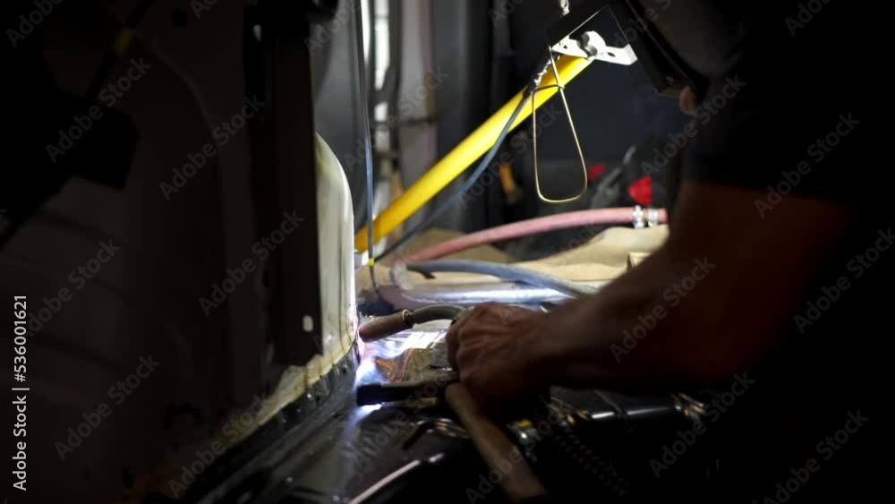 Poster an employee of a garage using a machine to weld inside of a car, protecting his face from the sparks