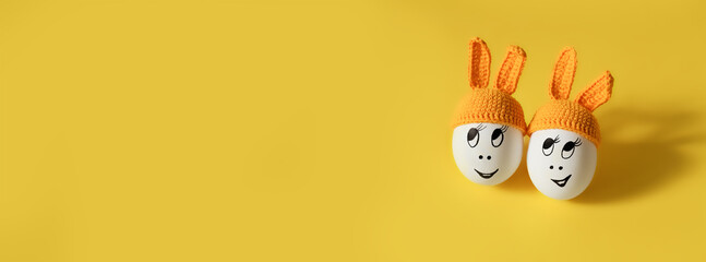 two white eggs in orange beanie with rabbit ears and cheerful faces on yellow background