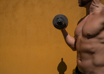 Young man working out lifting dumbbell outdoors during midday with harsh sunlight and yellow...