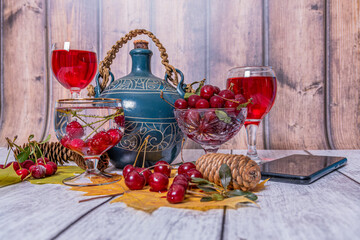 Jug,  glass filled with red wine, vase with ripe cherries, mobile phone lie on wooden table. Positive mood.