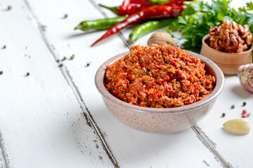 Adjika in a bowl on a white wooden table. Spicy sauce for meat dishes. Copy Space.