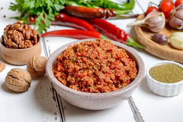 Adjika in a bowl and ingredients on a white wooden table. Georgian cuisine, spicy hot pepper sauce.