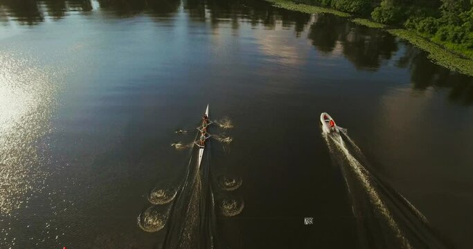 Drone shot on a sports canoe. Training of athletes in sports rowing on a kayak, a crew of four people rowing in calm water, a powerboat with a coach floats nearby. Ukraine. Kyiv.