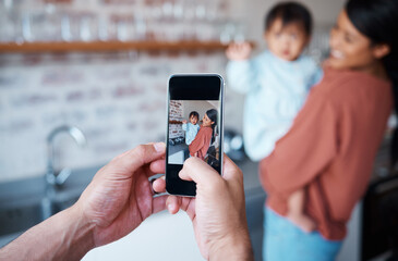 Fototapeta premium Father taking a picture of mother and baby on a phone in the kitchen of their family house. Love, care and man taking photo on smartphone of a happy and proud mom bonding with her child in their home