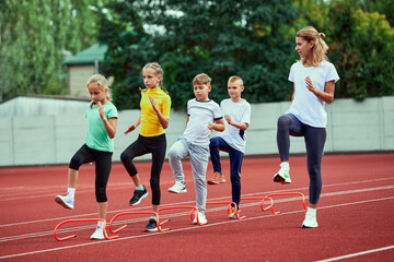 Female coach training athletes. Group of children running on treadmill at the stadium. Concept of sport, achievements, studying, goals, skills. Little boys and girls training outdoor. - Powered by Adobe