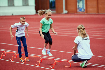 Female coach training athletes. Group of children running on treadmill at the stadium. Concept of...