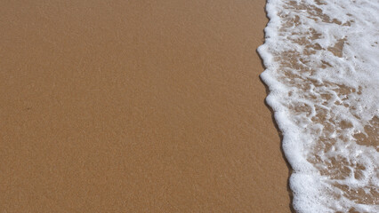 sea foam breaking on golden beach sand