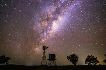 Milky Way rising over a windmill silhouette in a rural setting