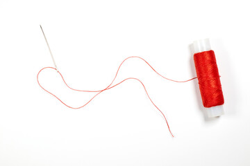 Needle with red thread and spool of thread on a white background