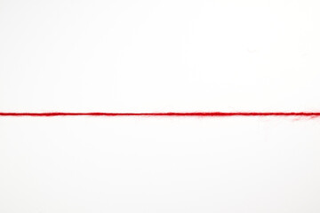 A straight line of red woolen threads on a white background