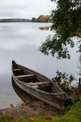 Obraz premium old wooden fishing boat stands on the lake in the village of autumn in cloudy weather.